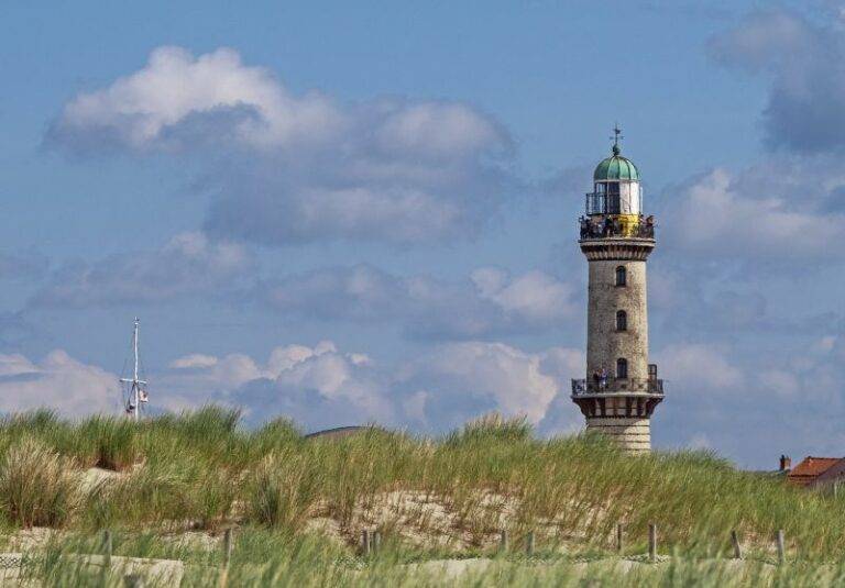 Der Leuchtturm Warnemünde erhebt sich aus den Dünen. Links davon der Mast eines Schiffes.