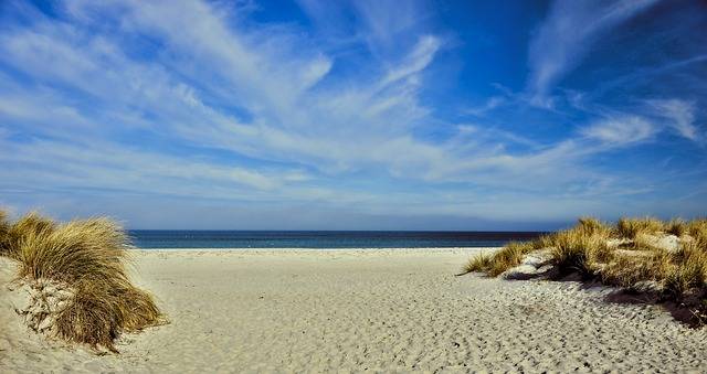 Die schönsten Strände der Ostsee während der Klassenfahrt besuchen. Auf dem Bild der Blick zwischen Dünen hindurch über den Strand auf das blaue Meer.